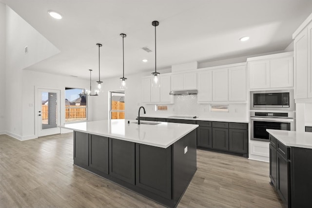 kitchen featuring white cabinetry, sink, oven, and an island with sink