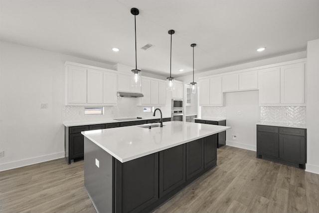 kitchen featuring sink, appliances with stainless steel finishes, white cabinetry, a center island with sink, and decorative light fixtures