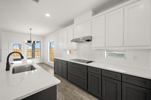 kitchen featuring sink, light hardwood / wood-style flooring, hanging light fixtures, backsplash, and black electric stovetop