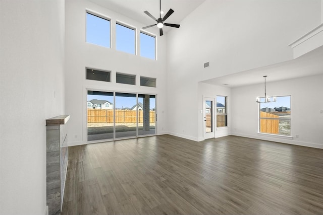 unfurnished living room featuring ceiling fan with notable chandelier, dark wood-type flooring, and a wealth of natural light