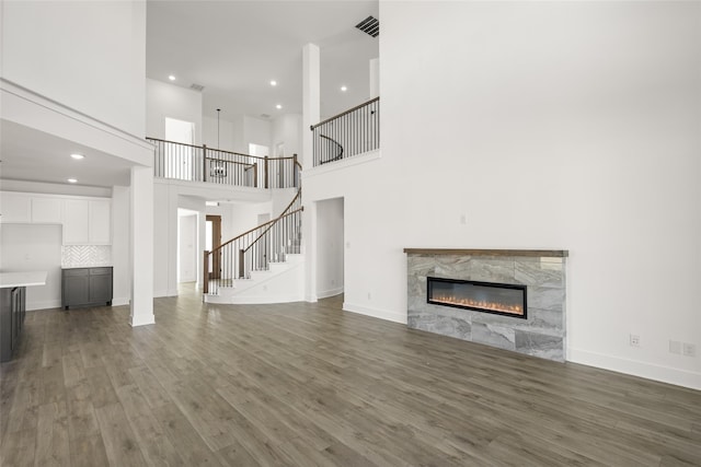 unfurnished living room featuring a high end fireplace, dark hardwood / wood-style floors, and a high ceiling