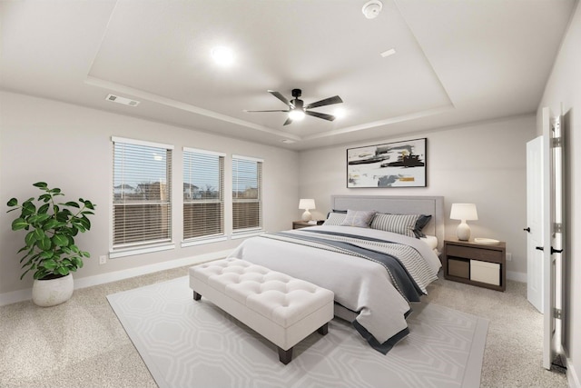 carpeted bedroom with ceiling fan and a raised ceiling