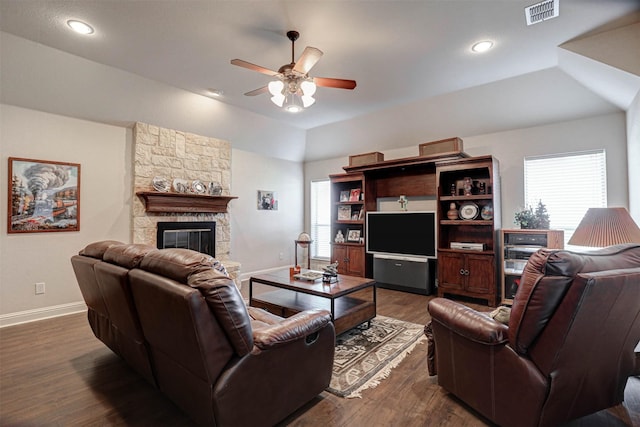 living room featuring a stone fireplace, dark wood-type flooring, visible vents, and baseboards