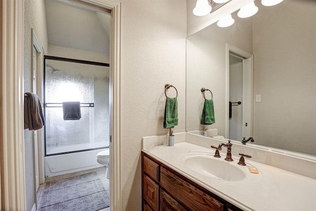 full bathroom featuring a textured wall, combined bath / shower with glass door, vanity, and toilet