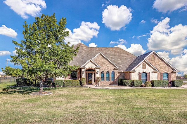 view of front of property with brick siding, a shingled roof, a front yard, fence, and stone siding