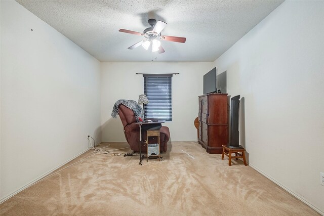 living area with ceiling fan, a textured ceiling, and light carpet