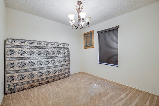 unfurnished room with a chandelier, a textured ceiling, and light carpet