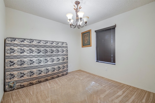 empty room with a notable chandelier, light colored carpet, and a textured ceiling