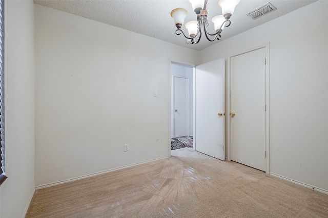 carpeted spare room with a textured ceiling and an inviting chandelier