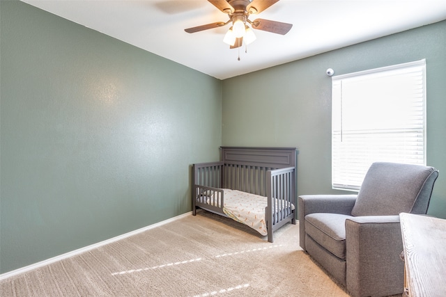 bedroom featuring a nursery area, light colored carpet, and ceiling fan