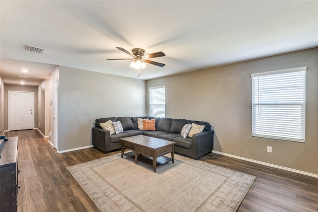 living room with a textured ceiling, ceiling fan, and dark wood-type flooring