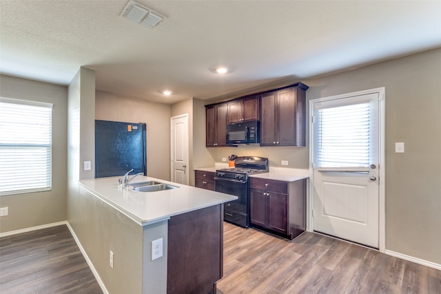 kitchen with kitchen peninsula, dark brown cabinets, sink, black appliances, and light hardwood / wood-style flooring