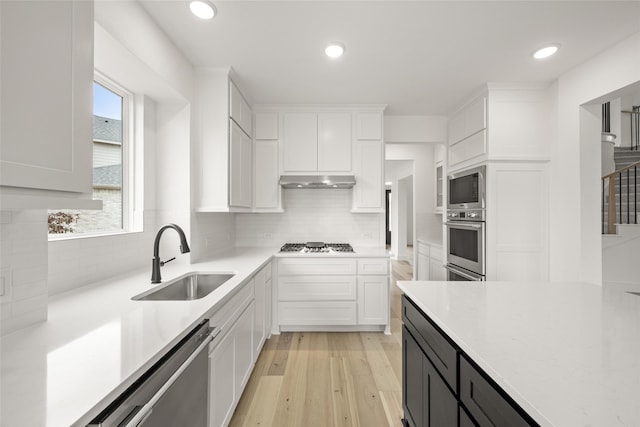 kitchen with light hardwood / wood-style flooring, appliances with stainless steel finishes, sink, white cabinets, and decorative backsplash