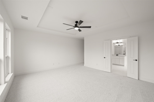 empty room featuring ceiling fan, a raised ceiling, and light carpet