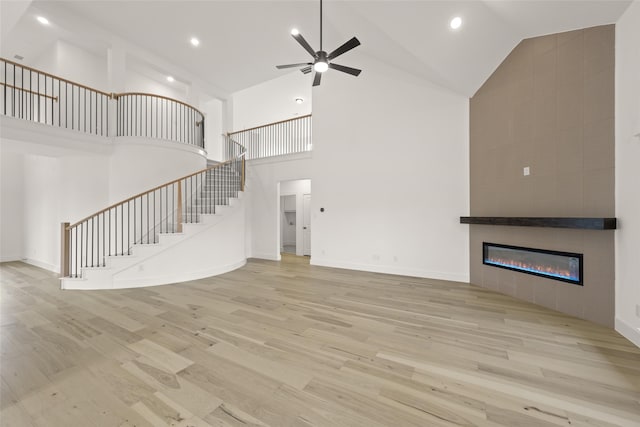 unfurnished living room with ceiling fan, a high ceiling, a tile fireplace, and light hardwood / wood-style flooring