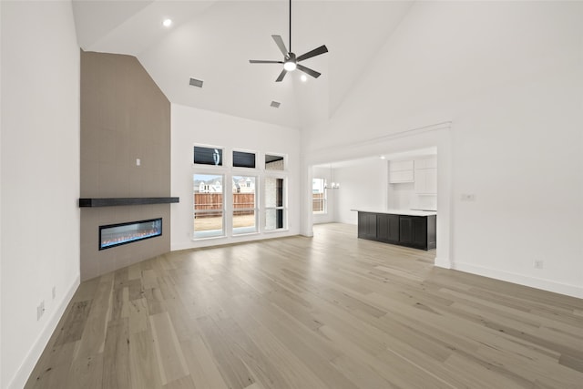 unfurnished living room with ceiling fan, high vaulted ceiling, light hardwood / wood-style flooring, and a fireplace