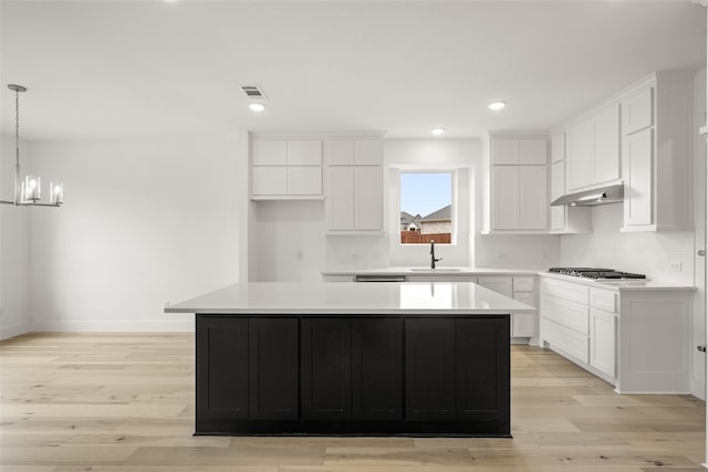 kitchen with sink, decorative light fixtures, white cabinets, a kitchen island, and light hardwood / wood-style floors