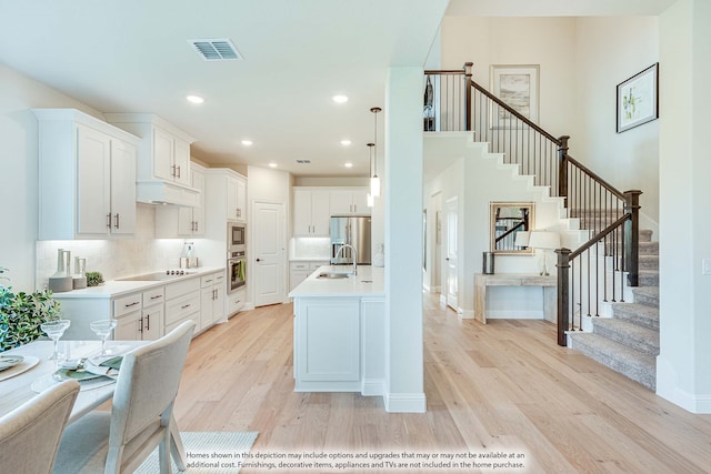 kitchen featuring pendant lighting, decorative backsplash, white cabinetry, light wood-type flooring, and appliances with stainless steel finishes