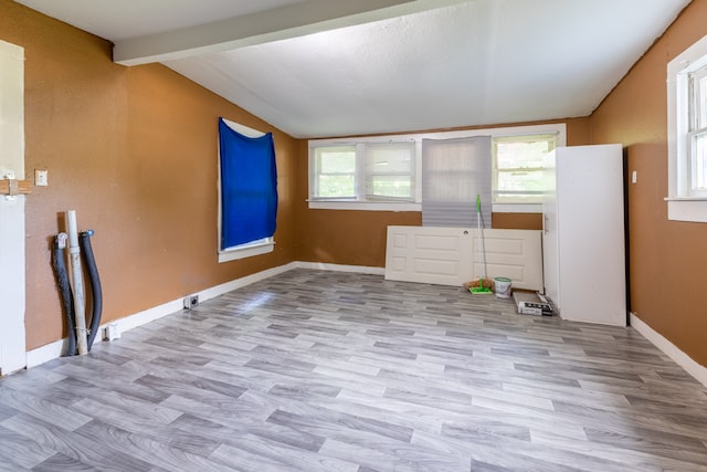 empty room featuring vaulted ceiling with beams, a healthy amount of sunlight, and light hardwood / wood-style floors