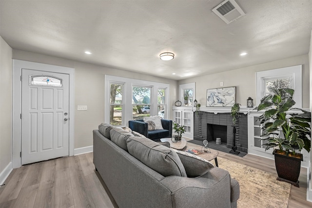 living room with light wood-type flooring, a textured ceiling, and a brick fireplace