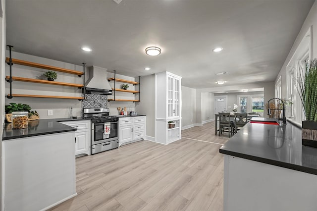 kitchen with white cabinets, stainless steel range with gas cooktop, sink, wall chimney exhaust hood, and light hardwood / wood-style floors