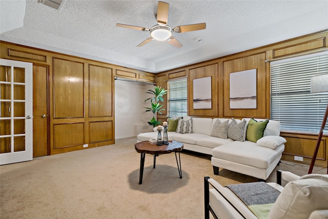 carpeted living room with wood walls, ceiling fan, and a textured ceiling