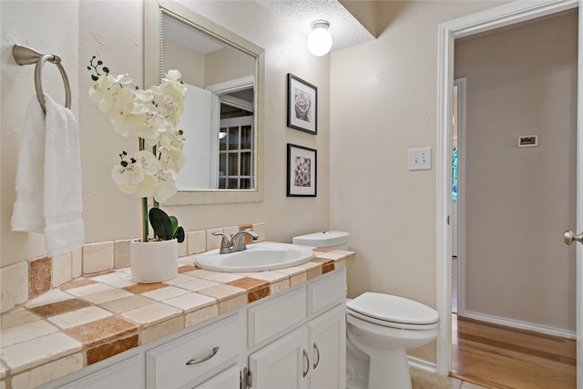 bathroom featuring vanity, wood-type flooring, a textured ceiling, and toilet