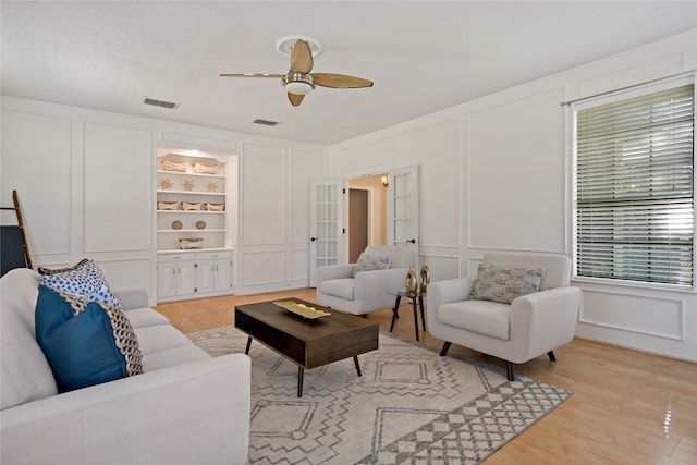 living room with built in shelves, ceiling fan, light hardwood / wood-style flooring, and a textured ceiling