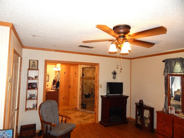 living room with crown molding, wood-type flooring, ceiling fan, and a textured ceiling