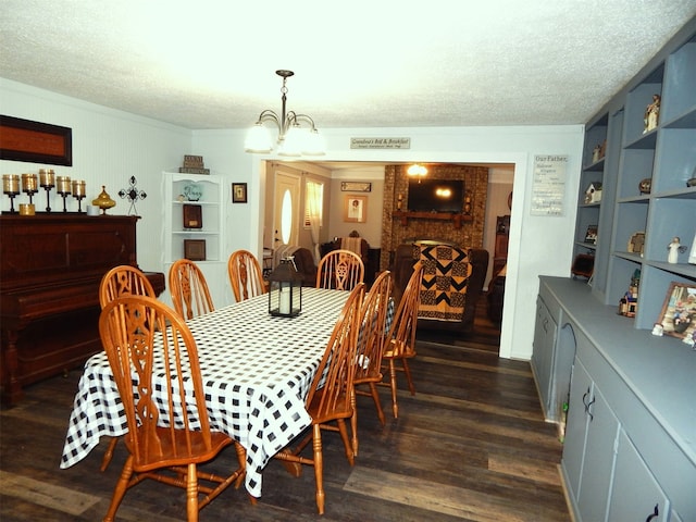 dining area with a brick fireplace, a chandelier, dark hardwood / wood-style floors, and a textured ceiling