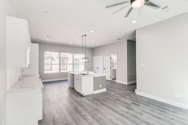 kitchen with wood-type flooring, white cabinetry, decorative light fixtures, sink, and a kitchen island with sink