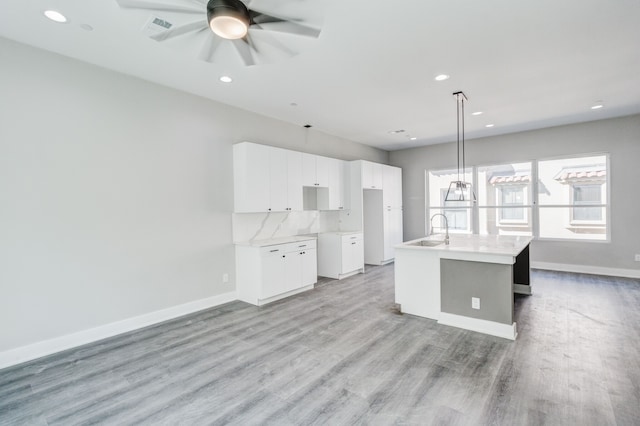 kitchen with sink, decorative light fixtures, an island with sink, white cabinets, and light wood-type flooring