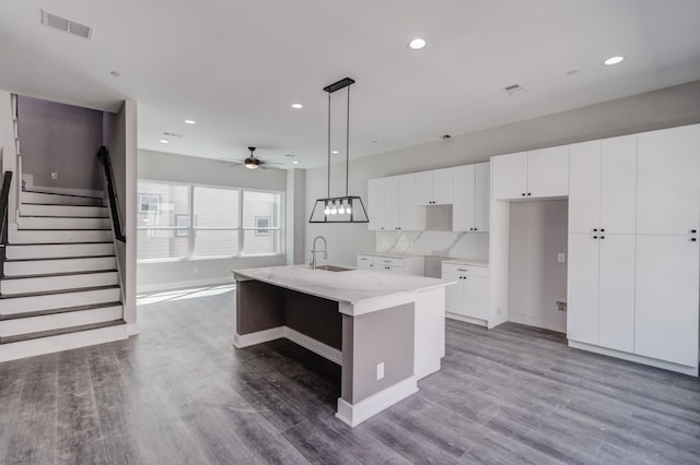 kitchen featuring a kitchen island with sink, hardwood / wood-style floors, white cabinets, and decorative light fixtures