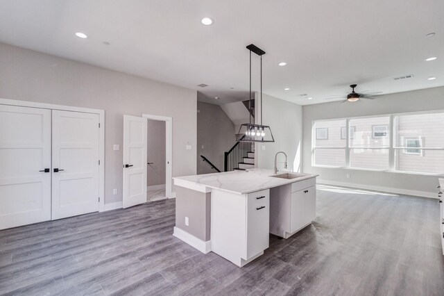 kitchen featuring hardwood / wood-style flooring, sink, an island with sink, white cabinetry, and decorative light fixtures