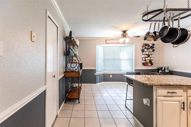 kitchen featuring light stone counters, ceiling fan, crown molding, light tile patterned floors, and white cabinetry