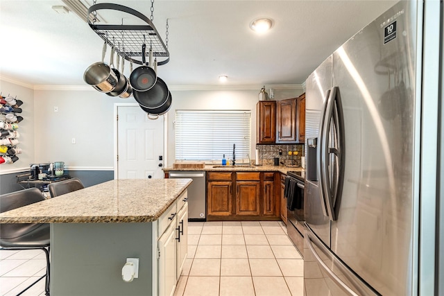 kitchen featuring light stone counters, stainless steel appliances, crown molding, light tile patterned floors, and a breakfast bar area