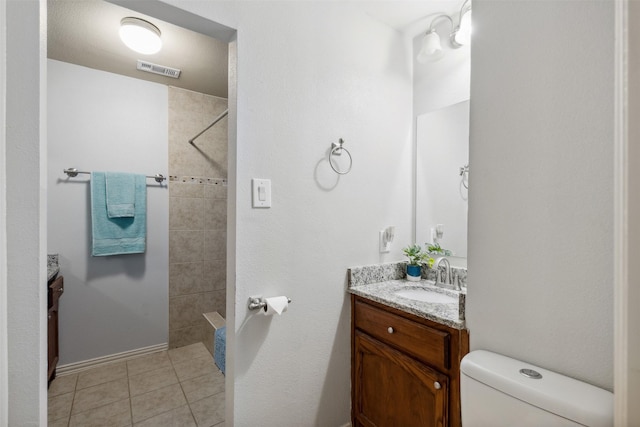 bathroom with toilet, tiled shower, vanity, and tile patterned floors