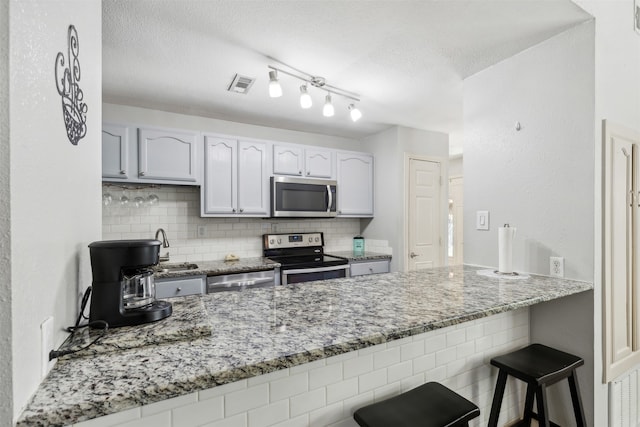 kitchen featuring white cabinetry, appliances with stainless steel finishes, backsplash, and light stone countertops