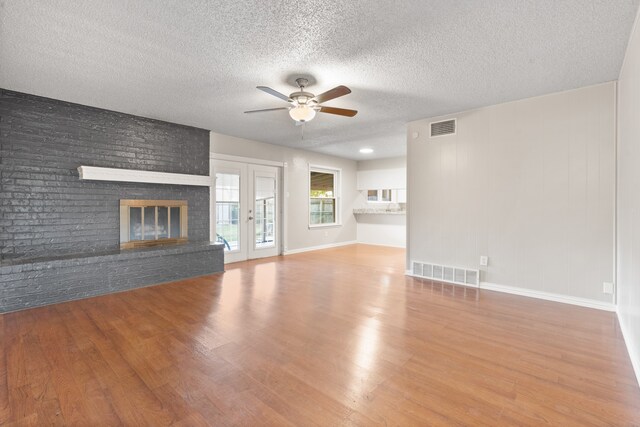 unfurnished living room with a textured ceiling, hardwood / wood-style flooring, french doors, and a brick fireplace