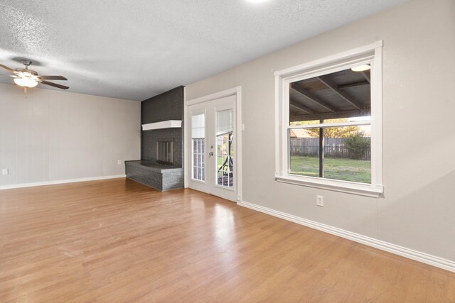 unfurnished living room with a fireplace, light hardwood / wood-style flooring, a textured ceiling, and ceiling fan