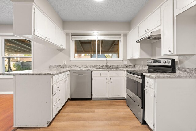 kitchen with stainless steel appliances, white cabinets, kitchen peninsula, sink, and light hardwood / wood-style flooring