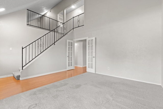 unfurnished living room featuring hardwood / wood-style floors, a towering ceiling, a textured ceiling, and french doors