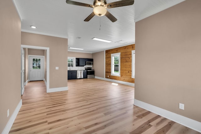 unfurnished living room featuring wood walls, ceiling fan, light hardwood / wood-style floors, and crown molding