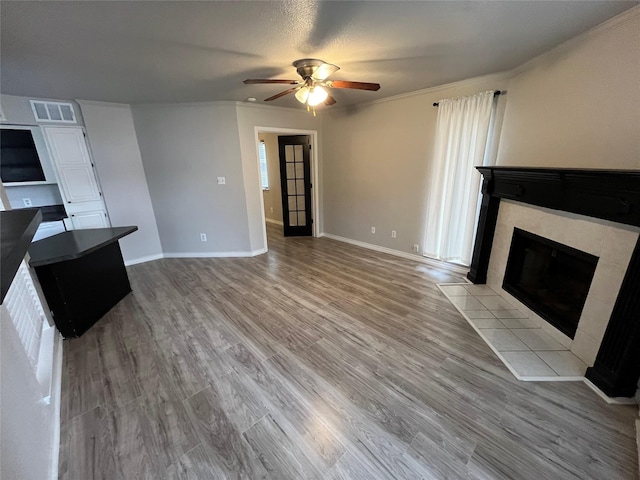 unfurnished living room with visible vents, a tiled fireplace, wood finished floors, baseboards, and ceiling fan