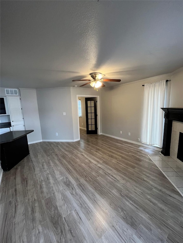 unfurnished living room with visible vents, ceiling fan, a tiled fireplace, wood finished floors, and a textured ceiling