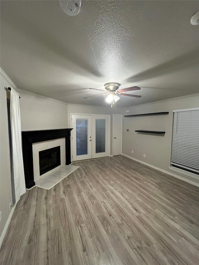 unfurnished living room featuring a fireplace with flush hearth, french doors, wood finished floors, a textured ceiling, and a ceiling fan