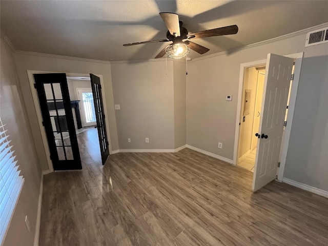 unfurnished room featuring visible vents, ornamental molding, wood finished floors, baseboards, and ceiling fan