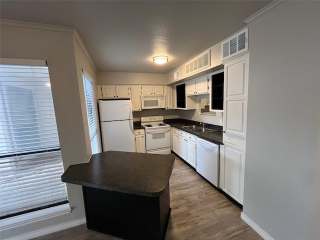 kitchen with visible vents, a sink, dark countertops, wood finished floors, and white appliances