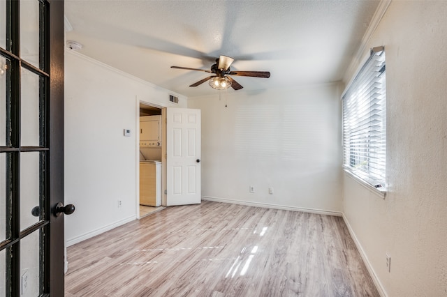 unfurnished room with stacked washer / dryer, light wood-type flooring, ceiling fan, and crown molding