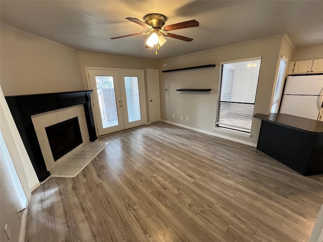 unfurnished living room featuring baseboards, ornamental molding, a tile fireplace, light wood-style floors, and a ceiling fan